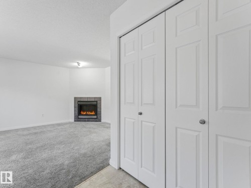 Living area featuring a fireplace with a dark tile surround and light grey carpet - 675 Mcallister Loop, Edmonton, AB - Indoor Photo Showing Other Room With Fireplace
