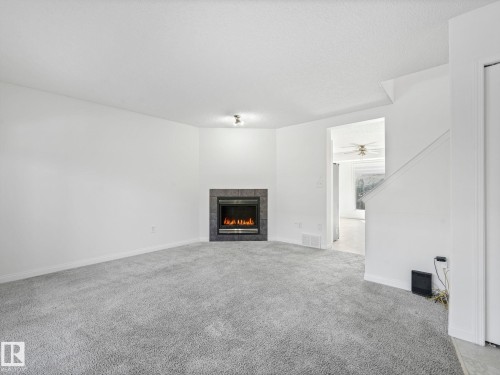 Living area with grey carpeting, white walls, and a corner fireplace featuring a dark stone surround - 675 Mcallister Loop, Edmonton, AB - Indoor Photo Showing Living Room With Fireplace