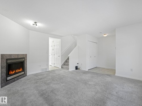 Living area featuring a fireplace with a tiled surround, grey carpeting, and light-colored walls - 675 Mcallister Loop, Edmonton, AB - Indoor With Fireplace