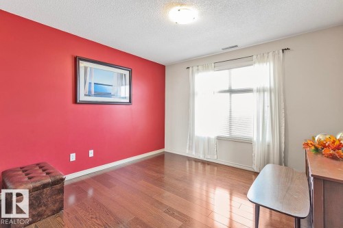 This space features rich hardwood flooring, a bright window with white sheer curtains, and a vibrant accent wall - 225 16035 132 Street, Edmonton, AB - Indoor Photo Showing Other Room