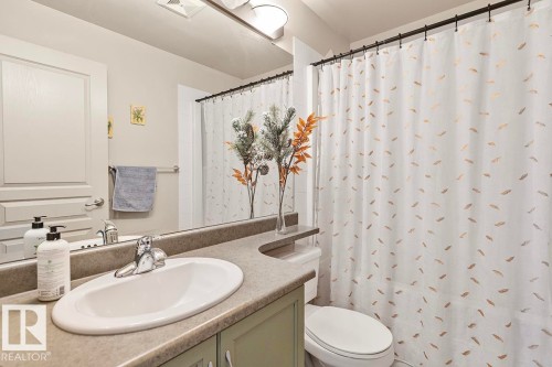 Bathroom featuring a vanity with an integrated sink, a mirror, and a shower with a decorative curtain - 225 16035 132 Street, Edmonton, AB - Indoor Photo Showing Bathroom