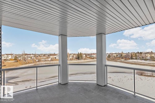 The property features a balcony with a gray floor and a glass railing, offering expansive views of the lake and surrounding homes - 225 16035 132 Street, Edmonton, AB - Outdoor