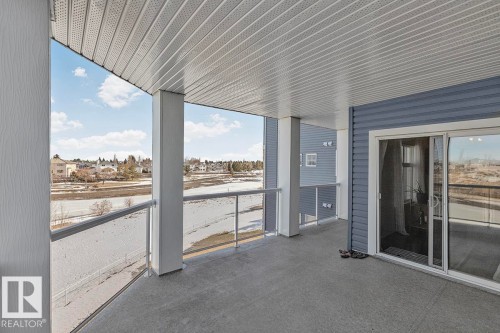 This property features a balcony with a concrete floor, white pillars, and a glass railing, providing views of the surrounding area - 225 16035 132 Street, Edmonton, AB - Outdoor With Exterior