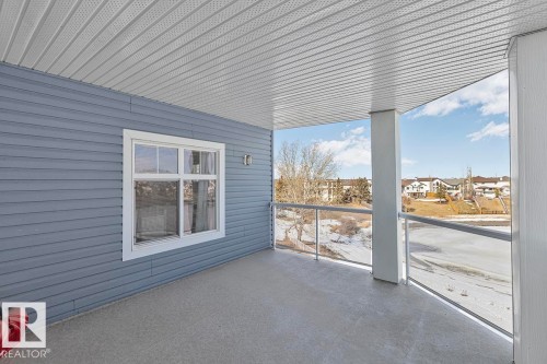 The property features a balcony with a textured floor, a white ceiling, and a blue exterior wall with a white-framed window - 225 16035 132 Street, Edmonton, AB -  With Exterior