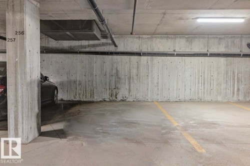 Underground parking space with concrete walls and ceiling, featuring fluorescent lighting and clearly marked parking lines - 225 16035 132 Street, Edmonton, AB - Indoor Photo Showing Garage