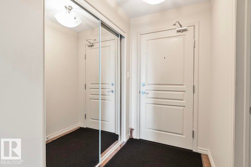 The entry features a white door, a full-length mirrored closet door, and overhead lighting fixtures - 225 16035 132 Street, Edmonton, AB - Indoor Photo Showing Other Room