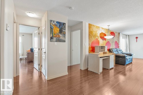 The property features hardwood floors throughout the main living areas, white walls, and a decorative accent wall with a floral design - 225 16035 132 Street, Edmonton, AB - Indoor Photo Showing Kitchen