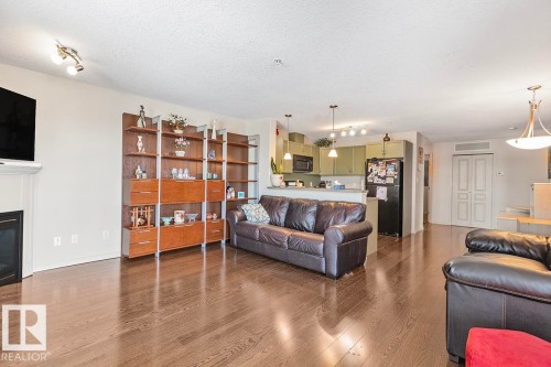 The living area features hardwood floors and a fireplace with a white mantel, alongside a built-in shelving unit - 225 16035 132 Street, Edmonton, AB - Indoor Photo Showing Living Room With Fireplace