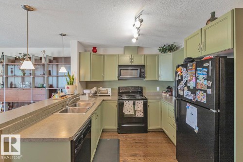The kitchen features light green cabinetry, a black oven and microwave, and a black refrigerator - 225 16035 132 Street, Edmonton, AB - Indoor Photo Showing Kitchen With Double Sink