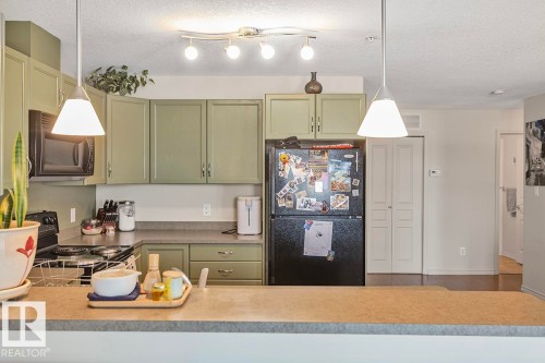 The kitchen features a U-shaped countertop layout, green cabinetry, and a black refrigerator - 225 16035 132 Street, Edmonton, AB - Indoor Photo Showing Kitchen
