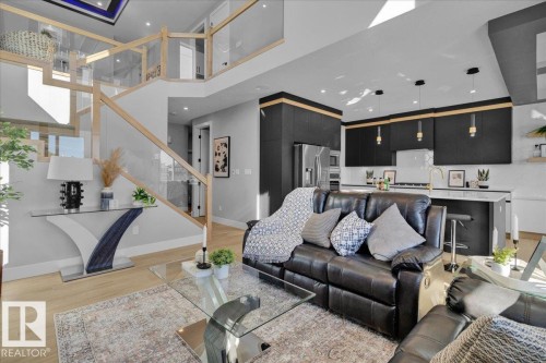 The property features an open-concept living area with light wood-look flooring, a modern kitchen with dark cabinetry, and a staircase with glass railings - 207 Starling, Fort Saskatchewan, AB - Indoor