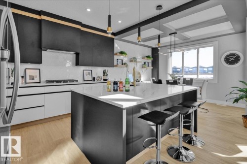 A modern kitchen featuring black and white cabinetry, a large island with a white countertop, and light wood flooring - 207 Starling, Fort Saskatchewan, AB - Indoor Photo Showing Kitchen With Upgraded Kitchen