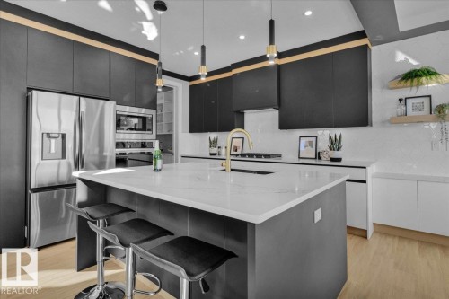 Modern kitchen featuring stainless steel appliances, a center island with seating, a gold-toned faucet, and dark cabinetry - 207 Starling, Fort Saskatchewan, AB - Indoor Photo Showing Kitchen With Upgraded Kitchen