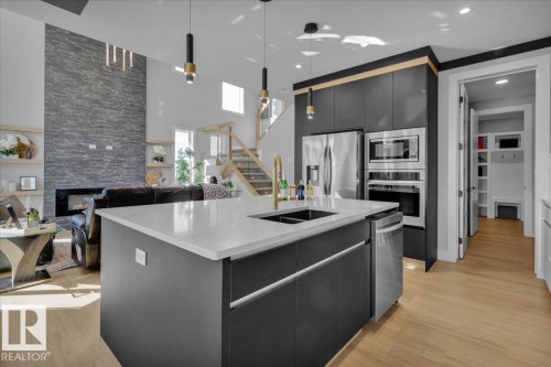 The kitchen features an island with a light-colored countertop and an integrated sink, dark cabinetry, and stainless steel appliances including an oven, microwave, and refrigerator - 207 Starling, Fort Saskatchewan, AB - Indoor Photo Showing Kitchen With Double Sink With Upgraded Kitchen