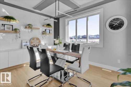 Dining area featuring a contemporary linear chandelier, light wood flooring, and a large window providing natural light and views of other properties - 207 Starling, Fort Saskatchewan, AB - Indoor Photo Showing Dining Room