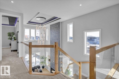 The property features a staircase with light wood railings and glass panels, a high ceiling with a modern chandelier, and recessed lighting - 207 Starling, Fort Saskatchewan, AB - Indoor Photo Showing Other Room