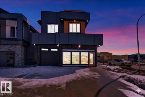 This contemporary property features a sleek dark exterior with stone accents and illuminated windows, presenting a modern aesthetic - 207 Starling, Fort Saskatchewan, AB - Outdoor