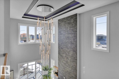 This soaring entryway features a modern chandelier, a decorative ceiling with accent lighting, and a textured stone wall - 207 Starling, Fort Saskatchewan, AB - Indoor Photo Showing Other Room
