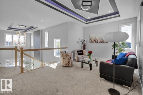 Spacious carpeted living area featuring a decorative ceiling with accent lighting, large windows providing natural light, and a glass panel railing overlooking the floor below - 207 Starling, Fort Saskatchewan, AB - Indoor Photo Showing Other Room