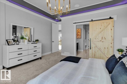 This room features a gold chandelier, an accent ceiling with purple lighting, and a barn door - 207 Starling, Fort Saskatchewan, AB - Indoor Photo Showing Bedroom