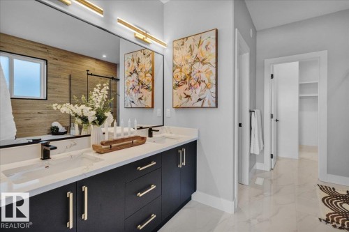 Bathroom vanity featuring double sinks, dark cabinetry with gold-toned hardware, and a large mirror with modern lighting - 207 Starling, Fort Saskatchewan, AB - Indoor Photo Showing Other Room