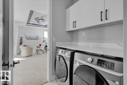 The property features a dedicated laundry area with white upper cabinetry, a white countertop, and modern front-loading laundry machines - 207 Starling, Fort Saskatchewan, AB - Indoor Photo Showing Laundry Room