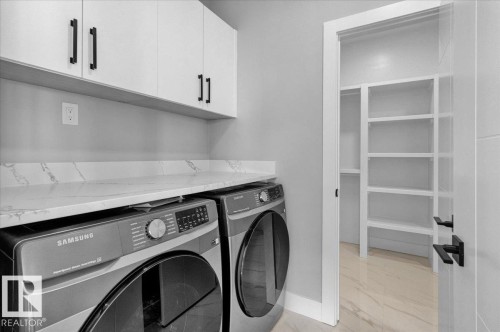 Laundry area featuring white cabinetry with dark handles, a light-colored countertop, and a built-in shelving unit - 207 Starling, Fort Saskatchewan, AB - Indoor Photo Showing Laundry Room