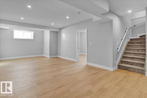 Spacious room featuring light-toned flooring, recessed lighting, a window, and a carpeted staircase with a white handrail - 207 Starling, Fort Saskatchewan, AB - Indoor Photo Showing Other Room