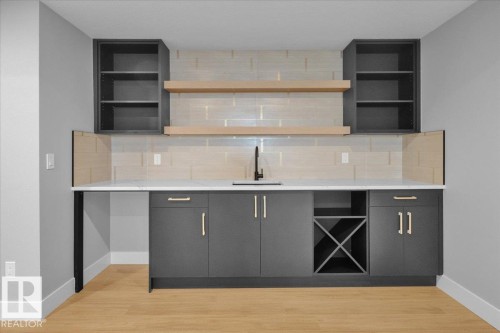 A well-appointed wet bar area featuring a sink with a black faucet, grey cabinetry with gold-toned hardware, and light wood open shelving - 207 Starling, Fort Saskatchewan, AB - Indoor Photo Showing Kitchen With Upgraded Kitchen