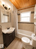 Bathroom featuring a wood-panel ceiling, tiled shower surround with decorative accent band, and a white framed window - 