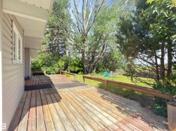 Expansive wood deck with a partial railing, offering direct access to a grassy yard featuring mature trees and lush greenery - 