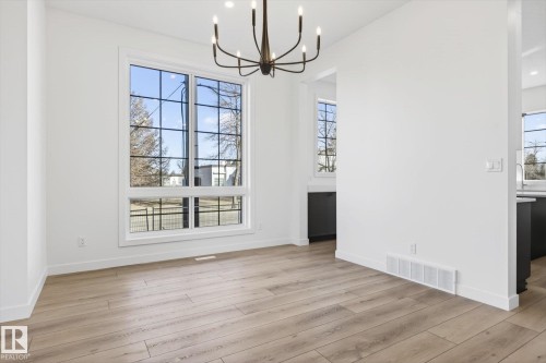 This spacious room features light wood flooring, white walls, and a large window with black grilles - 9705 68 Avenue, Edmonton, AB - Indoor Photo Showing Other Room