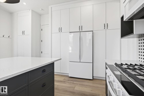 The property features an open-concept kitchen with a large central island, white cabinetry, and light wood flooring - 9705 68 Avenue, Edmonton, AB - Indoor Photo Showing Kitchen