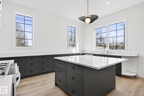 The kitchen features white walls, dark cabinetry with dark hardware, a large kitchen island with a white countertop, and light-toned flooring - 9705 68 Avenue, Edmonton, AB - Indoor Photo Showing Kitchen