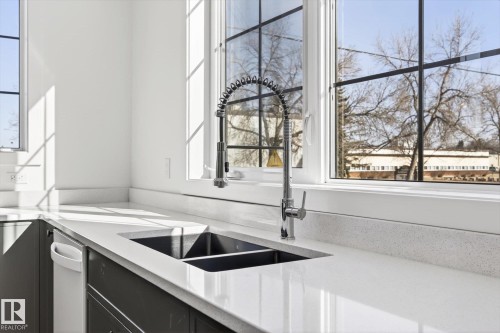 Kitchen featuring a double basin sink with a modern pull-down faucet, white countertops, and dark lower cabinets - 9705 68 Avenue, Edmonton, AB - Indoor Photo Showing Kitchen With Double Sink