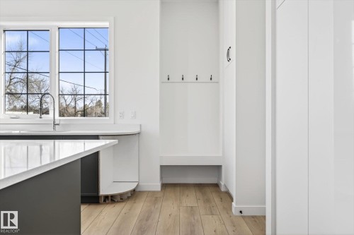 Kitchen featuring a large window with gridded panes, a sink with a gooseneck faucet, light wood flooring, and white cabinetry - 9705 68 Avenue, Edmonton, AB - Indoor Photo Showing Other Room
