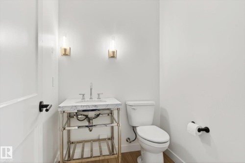 Bathroom with a white toilet, a vanity with a white countertop and a silver base, and two wall-mounted light fixtures - 9705 68 Avenue, Edmonton, AB - Indoor Photo Showing Bathroom