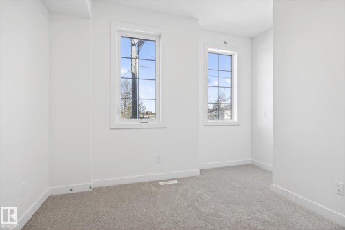 The room features two windows with gridded panes, light gray carpet, and white baseboards - 9705 68 Avenue, Edmonton, AB - Indoor Photo Showing Other Room