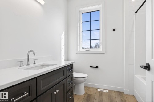 Bathroom featuring a dark wood vanity with a white countertop and chrome faucet, a window providing natural light, and wood-style flooring - 9705 68 Avenue, Edmonton, AB - Indoor Photo Showing Bathroom