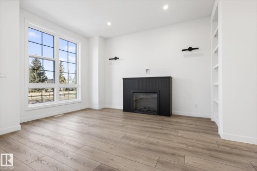 This bright room features a large window with grid pattern, light-toned flooring, a black fireplace, and built-in shelving - 9705 68 Avenue, Edmonton, AB - Indoor Photo Showing Living Room With Fireplace