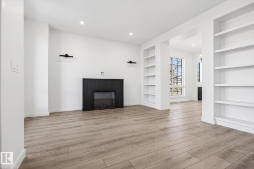 The living area features light-colored flooring, a dark fireplace, and recessed lighting - 9705 68 Avenue, Edmonton, AB - Indoor With Fireplace