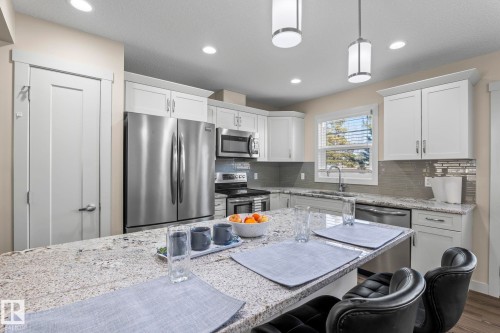 The kitchen features a spacious island with a granite countertop, white cabinetry, and stainless steel appliances - 24 4205 30 Street, Edmonton, AB - Indoor Photo Showing Kitchen With Stainless Steel Kitchen