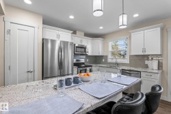 The kitchen features a spacious island with a granite countertop, white cabinetry, and stainless steel appliances - 