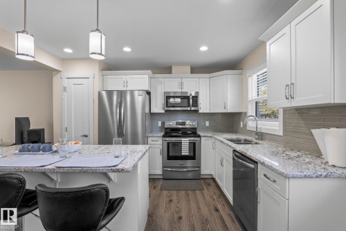 The kitchen features white cabinetry, stainless steel appliances, speckled countertops, and a gray tiled backsplash - 24 4205 30 Street, Edmonton, AB - Indoor Photo Showing Kitchen With Stainless Steel Kitchen With Double Sink With Upgraded Kitchen