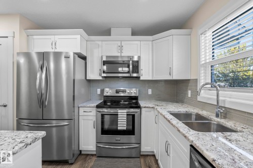 The kitchen features stainless steel appliances, white cabinetry, granite countertops, and a subway tile backsplash - 24 4205 30 Street, Edmonton, AB - Indoor Photo Showing Kitchen With Stainless Steel Kitchen With Double Sink With Upgraded Kitchen