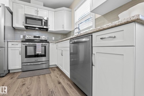 The kitchen features white cabinetry, granite countertops, stainless steel appliances, and a tiled backsplash - 24 4205 30 Street, Edmonton, AB - Indoor Photo Showing Kitchen With Stainless Steel Kitchen