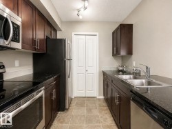 The kitchen features dark wood cabinetry, stainless steel appliances, dark countertops, a double basin sink, and tiled flooring - 