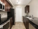 The kitchen features dark wood cabinetry, stainless steel appliances, dark countertops, a double basin sink, and tiled flooring - 209 107, Watt Commom, Edmonton, AB 