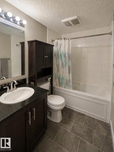 Bathroom featuring a vanity with a white sink, a dark countertop, and dark cabinetry - 209 107, Watt Commom, Edmonton, AB 