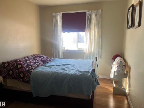 The room features a window with white curtains, light-colored walls, and wood-style flooring - 55131 Range Road 83, Rural Yellowhead, AB - Indoor Photo Showing Bedroom